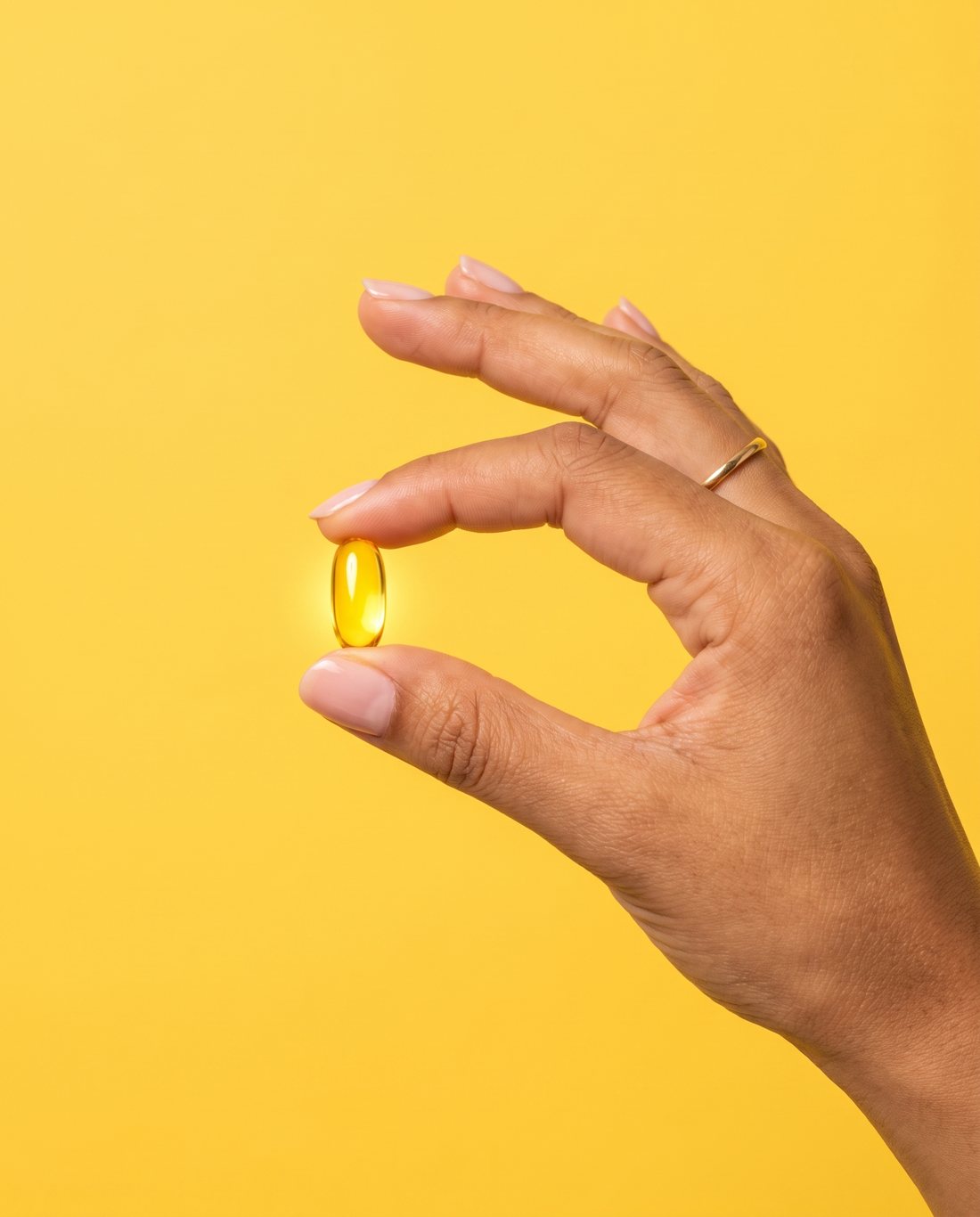 Two golden liquid capsules in a hand with the Sakoon bottle behind